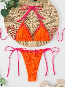 Vibrant orange ribbed halter bikini set with pink lace-up detailing on woven mat background