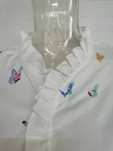 Close-up of ruffled lotus collar and colorful butterfly prints on white blouse.