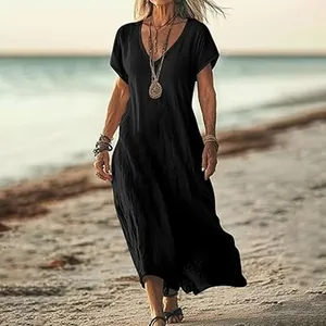 Model wearing a black loose V-neck cotton linen maxi dress walking on a sunny beach