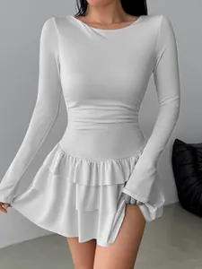 Detail view of a white long-sleeved slim fit mini dress with ruffled hem and pleated waist.