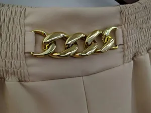 Detail van de gouden kettingversiering op beige damesbroeken met wijde pijpen en elastische taille