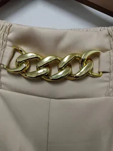 Detail van de gouden ketting decoratie op een beige damesbroek met wijde pijpen