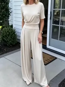 Woman in elegant cream short-sleeved top and matching pleated wide-leg trousers set.