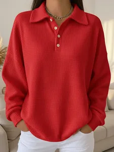 Detail shot of a vibrant red waffle-knit long-sleeved polo shirt with white buttons