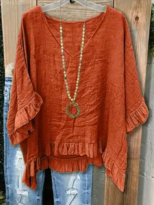 Detailansicht der orangefarbenen Damenbluse mit V-Ausschnitt, Volantsaum und Strukturstoff.