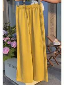 Detail of yellow wide-leg drawstring trousers hanging in a sunny outdoor cafe setting