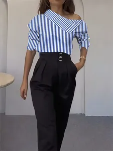 Détail d'une chemise à épaules dénudées à rayures bleues et d'un pantalon noir.