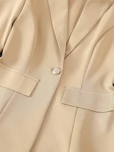 Detailansicht der beigen Blazerstruktur und des verzierten goldenen Knopfs