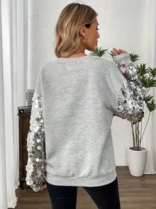 Vista posteriore di una felpa grigia festiva con maxi paillettes argento sulle maniche.