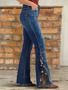 Close-up view of flared denim jeans with colorful floral embroidery details on the side