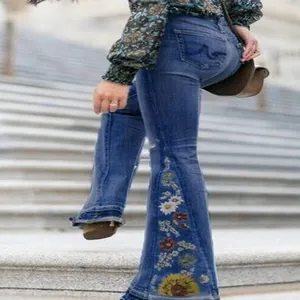 Close-up detail of colorful floral embroidery on stylish blue denim flare jeans for women.