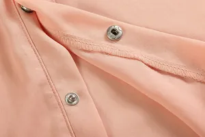 Détail des boutons-pression métalliques et des coutures sur une robe rose pêche en mousseline