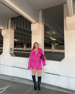 Model wearing a vibrant pink pleated long-sleeve shirt dress in an urban setting