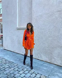 Close-up detail of a vibrant orange pleated long-sleeve shirt dress with a waist tie belt