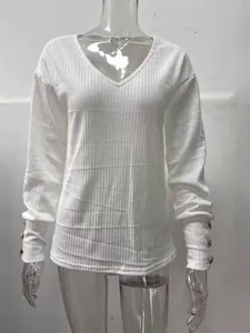 Dettaglio maglia bianca scollo V con trama a coste e bottoni dorati decorativi sui polsini