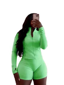 Femme portant un ensemble de sport vert citron avec veste et short, selfie en pied sur blanc.