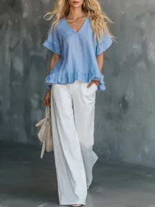 Schicke hellblaue Rüschenbluse mit V-Ausschnitt und weißer Leinenhose mit weitem Bein.