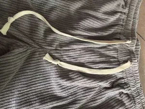 Close-up detail shot of grey corduroy trousers showing fabric texture and drawstring tie.