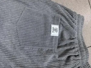 Detailed close-up of grey corduroy pants showing vertical stripes and a white pocket label