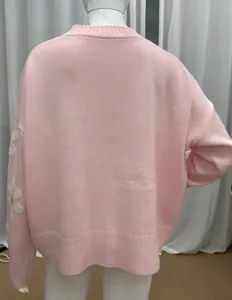 Vista posteriore di un cardigan in maglia rosa ampio con motivo a margherita sulla manica
