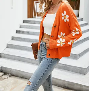 Vista dettagliata di un cardigan in maglia arancione con motivo a margherite e jeans