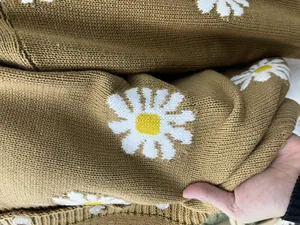 Makroansicht der Strickstruktur eines braunen Cardigans mit Gänseblümchen.