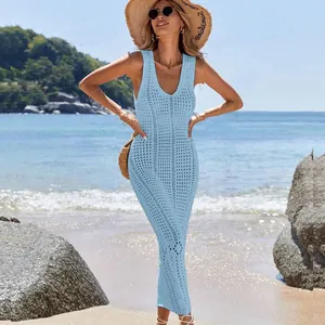 Model wearing a light blue hollow-out knit dress in a sunny beach and ocean setting.