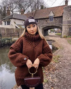 Detail view of a chunky brown turtleneck sweater with puffed long sleeves in a scenic setting