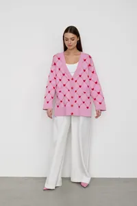 Full-body model shot featuring a pink V-neck cardigan with red heart jacquard patterns.