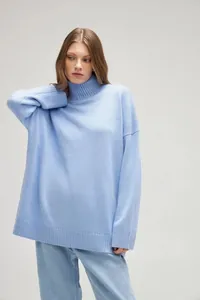 Female model wearing an oversized light blue turtleneck knit sweater in a studio setting