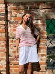 Model wearing a pink and white striped polo collar knit sweater in a sunny outdoor setting