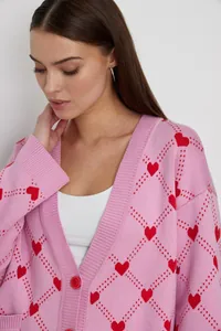 Close-up detail of a soft pink knit cardigan featuring a red heart and argyle jacquard pattern