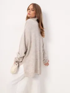 Oversized beige knit turtleneck sweater with side slits, shown from a rear side angle