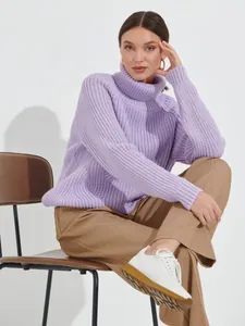 Detailed view of a woman wearing a purple chunky turtleneck knit sweater and brown pants