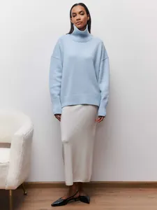Modèle portant un pull à col roulé bleu clair et une longue jupe en maille blanche
