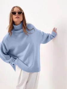 Close-up of a cozy oversized blue turtleneck sweater on a model with white pants