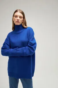 Female model wearing an oversized cobalt blue mock neck knitted sweater with ribbed cuffs.