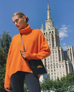 Model wearing an orange oversized turtleneck sweater with an urban building background