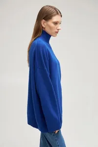 Side profile of woman wearing an oversized royal blue mock neck knit sweater