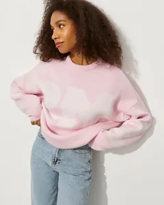 Frau trägt einen lockeren rosa-weißen Strickpullover mit großem Buchstaben-Design und Jeans