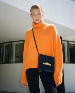 Model wearing vibrant orange oversized turtleneck sweater and black box crossbody bag