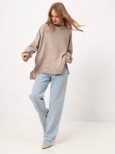 Full-body view of a woman wearing a loose beige turtleneck sweater and light blue jeans