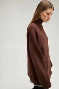 Side profile view showing the loose fit and textured knit of the brown turtleneck sweater.