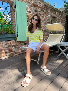 Woman wearing a yellow striped polo knit sweater and white shorts in a sunny outdoor setting