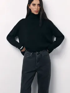 Detailed view of an oversized black turtleneck knit sweater featuring long ribbed cuffs.