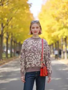 Stylish woman wearing a leopard print knit sweater and red handbag among golden autumn trees.