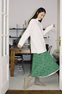 Model wearing a loose white half-turtleneck knit sweater and green leopard midi skirt.