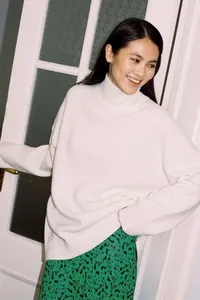 Elegant Asian model wearing an oversized white high-neck knit sweater in a cozy indoor setting