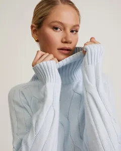 Close-up detail of light blue cable knit turtleneck sweater showing premium texture and finish