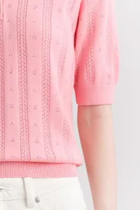 Detail view of a pink short-sleeved knit polo shirt with pointelle and cable texture